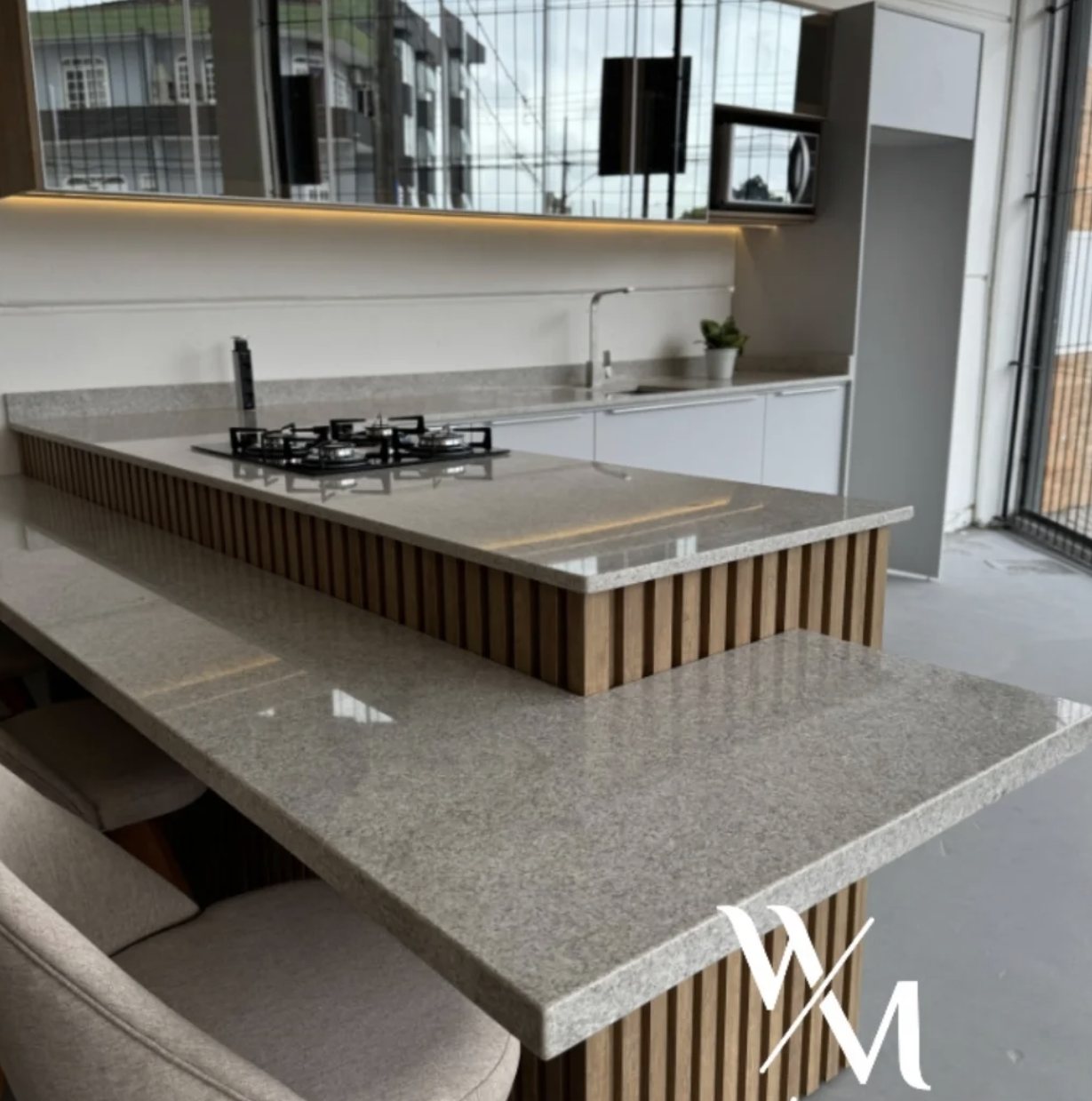Ilha de cozinha em pedra clara com cooktop e mesa de apoio no mesmo material